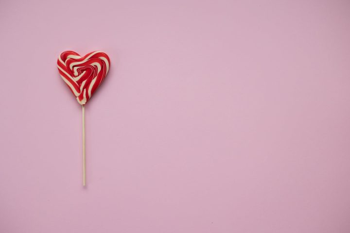 sweet lollipop in form of heart on pink background